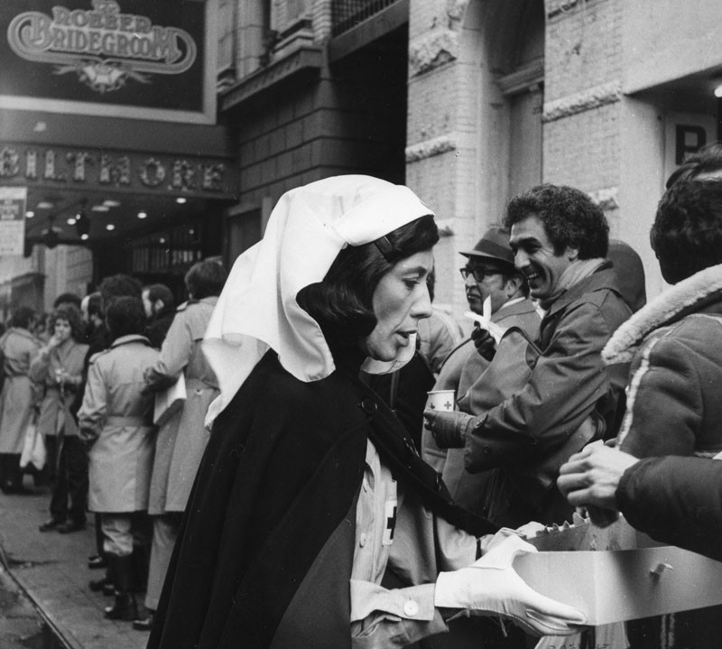 Lily Tomlin as “Red Cross Worker”. Handing out coffee and donuts to fans waiting in line to buy tickets to “Appearing Nitely” at the Biltmore. Young Judith Beasley “Stay Put” hair commercial from Emmy award winning special.  © 2015 Lily Tomlin. All Rights Reserved.